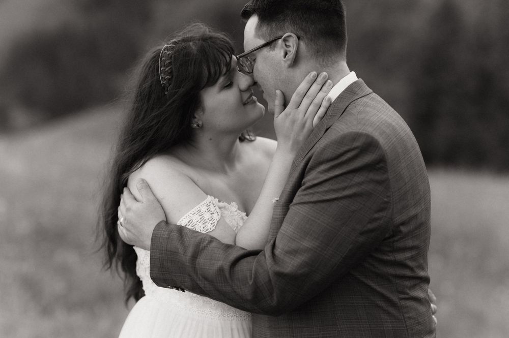 Black and white photo of a couple sharing a romantic embrace, nearly kissing, at an outdoor wedding ceremony.