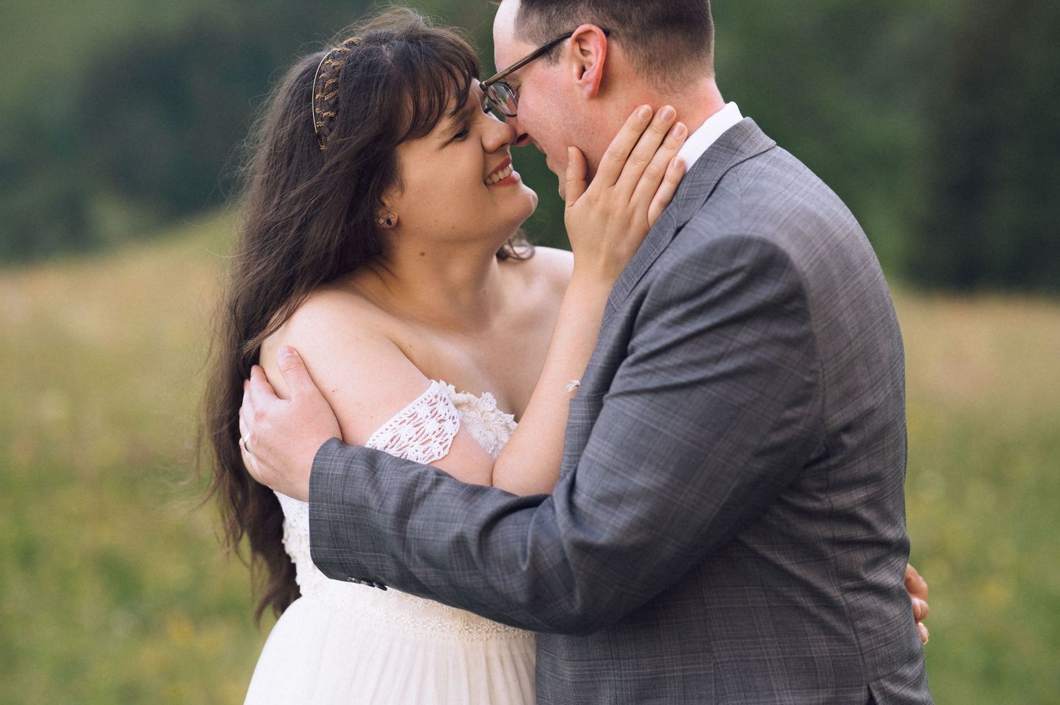 A bride and groom share a romantic moment, nearly kissing in a lush green field on their wedding day.