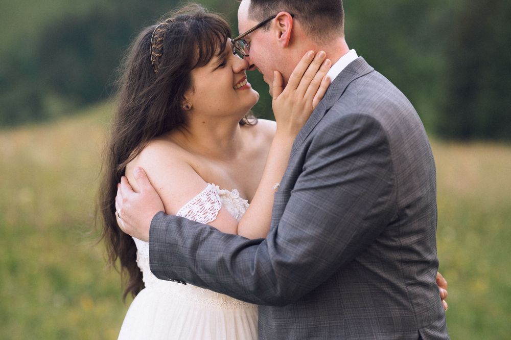 A bride and groom share a romantic moment, nearly kissing in a lush green field on their wedding day.