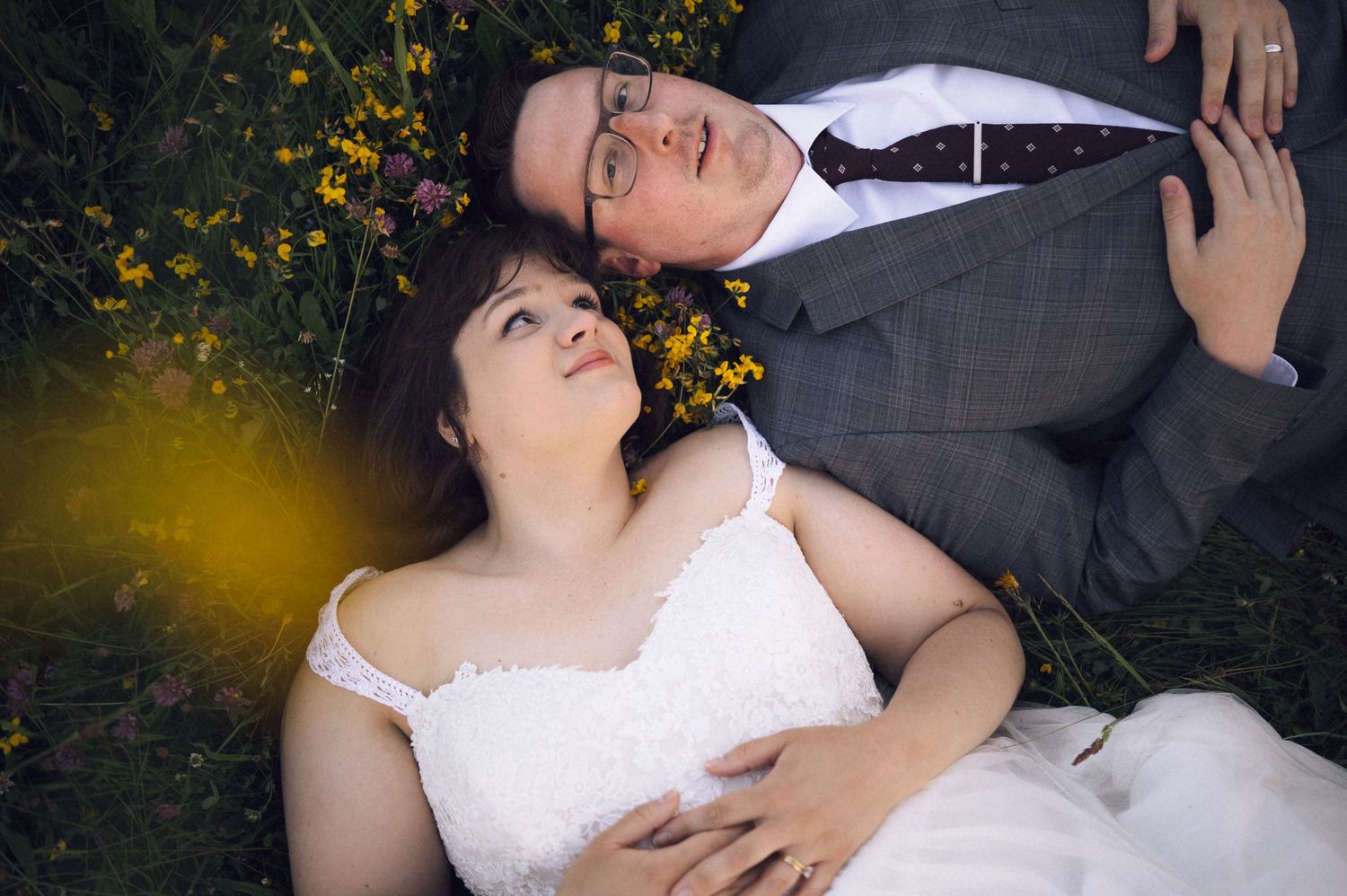 Bride and groom lying in a flower field, sharing a romantic moment in wedding attire.