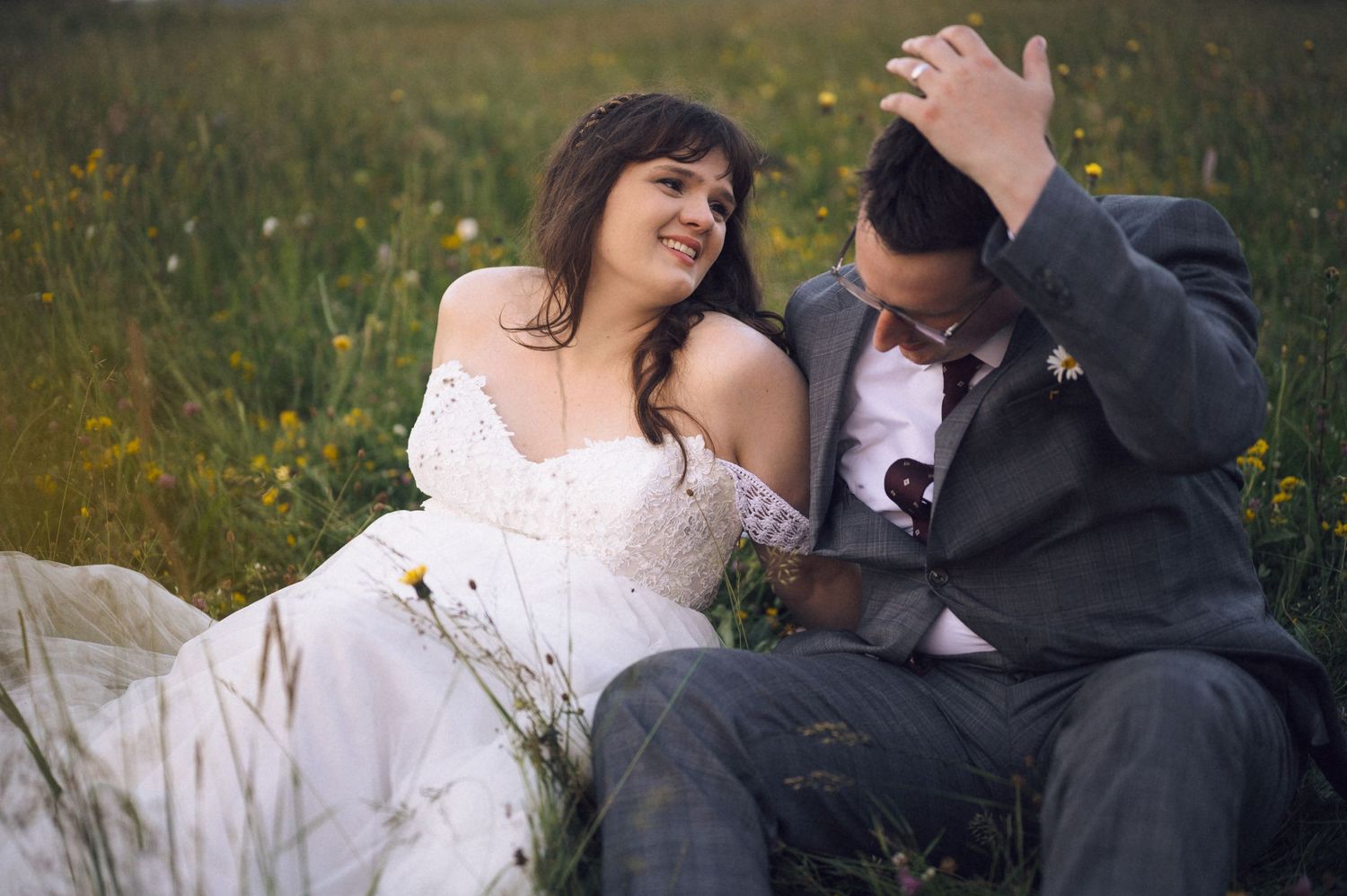 Bride and groom sitting together in a wildflower field, sharing a tender moment on their wedding day.