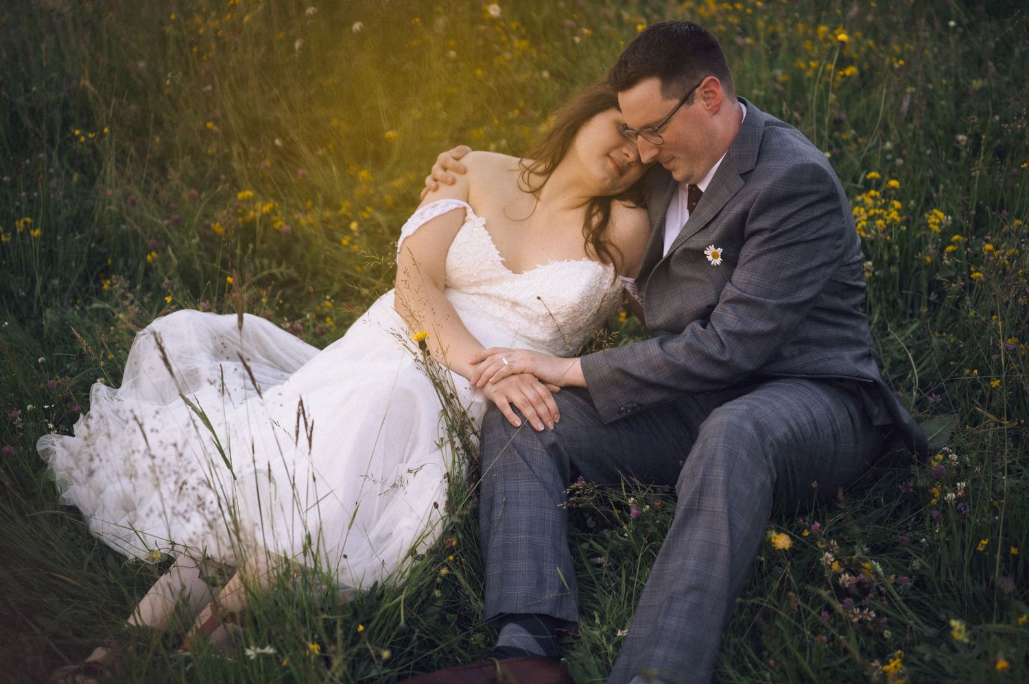 Bride and groom sitting together in a wildflower meadow, sharing an intimate moment in wedding attire.