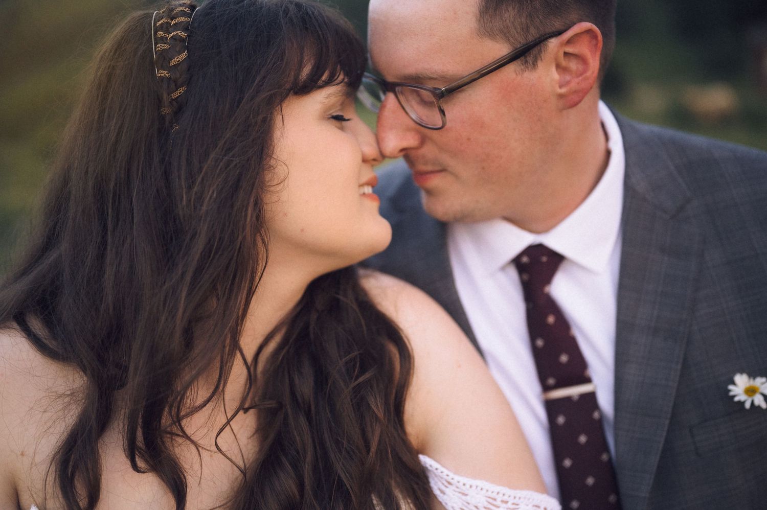 A couple shares a romantic almost-kiss moment, the woman wearing a floral headband and the man in glasses and a suit.