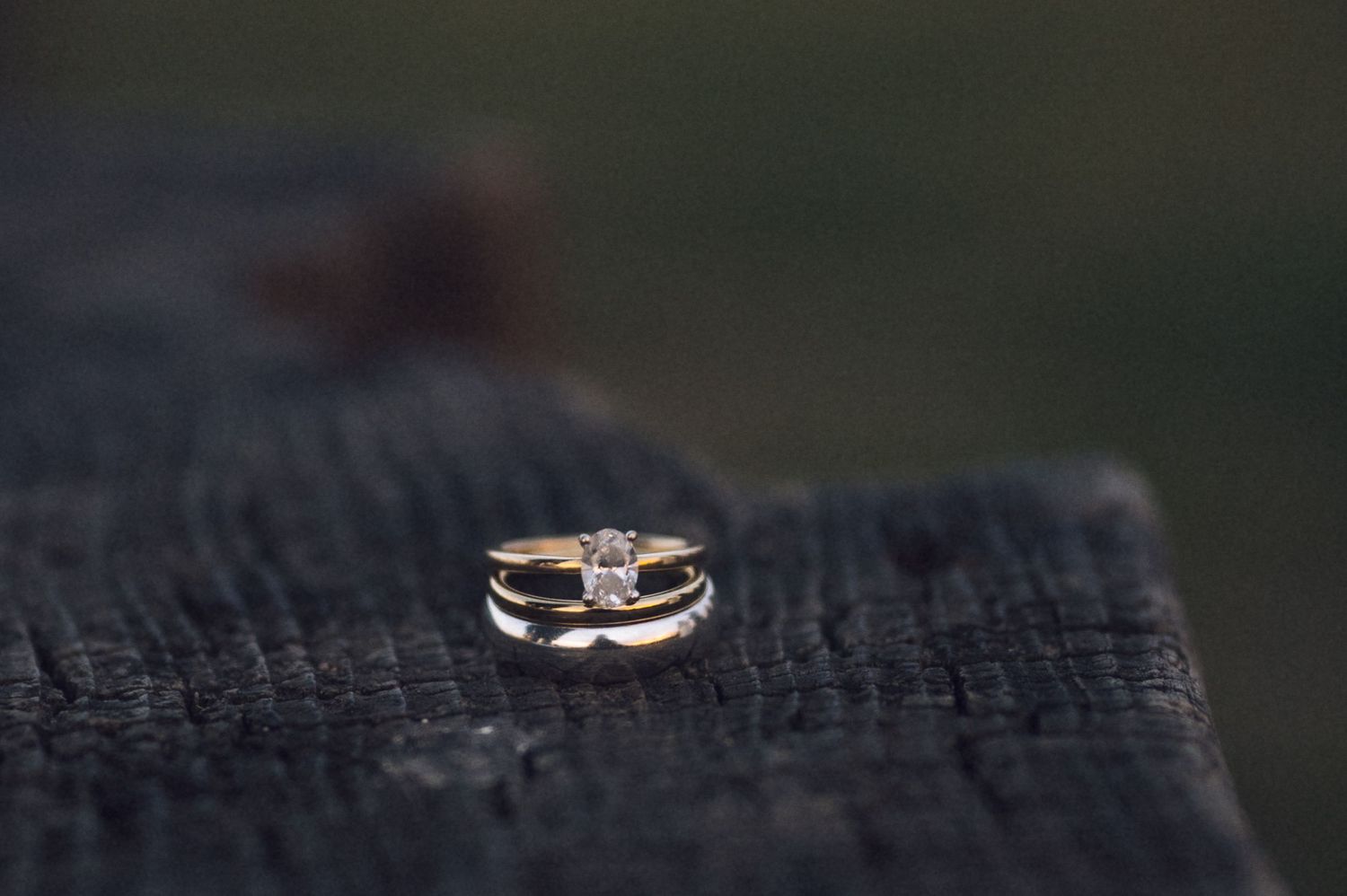 Gold wedding ring set with diamond solitaire resting on rustic dark wood surface.
