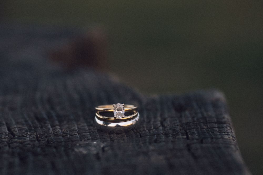 Gold wedding ring set with diamond solitaire resting on rustic dark wood surface.