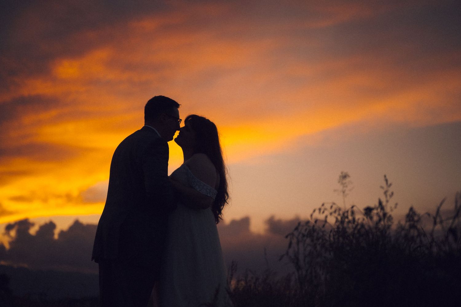 Romantic couple silhouette sharing a kiss against a vibrant orange and red sunset sky.