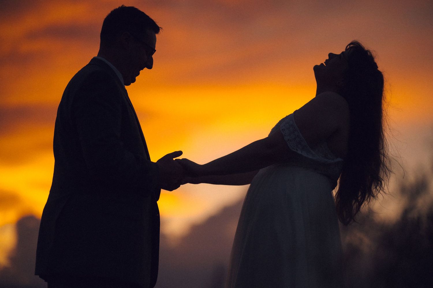 Silhouette of a couple holding hands at sunset with vibrant orange sky backdrop.