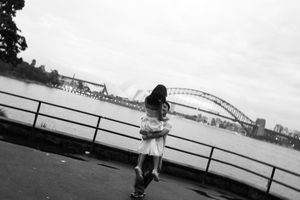 Couple embracing by Sydney Harbour Bridge waterfront in black and white photo on overcast day.