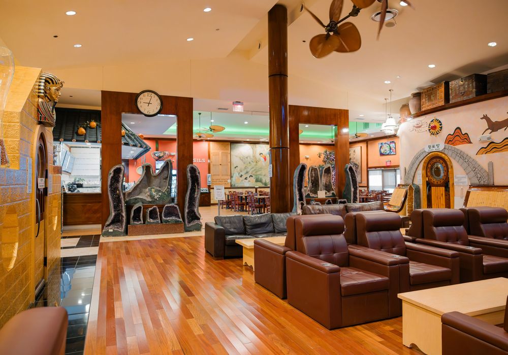 Spacious hotel lounge with hardwood floors, leather chairs, wooden columns, and eclectic decor including wall art and a clock.