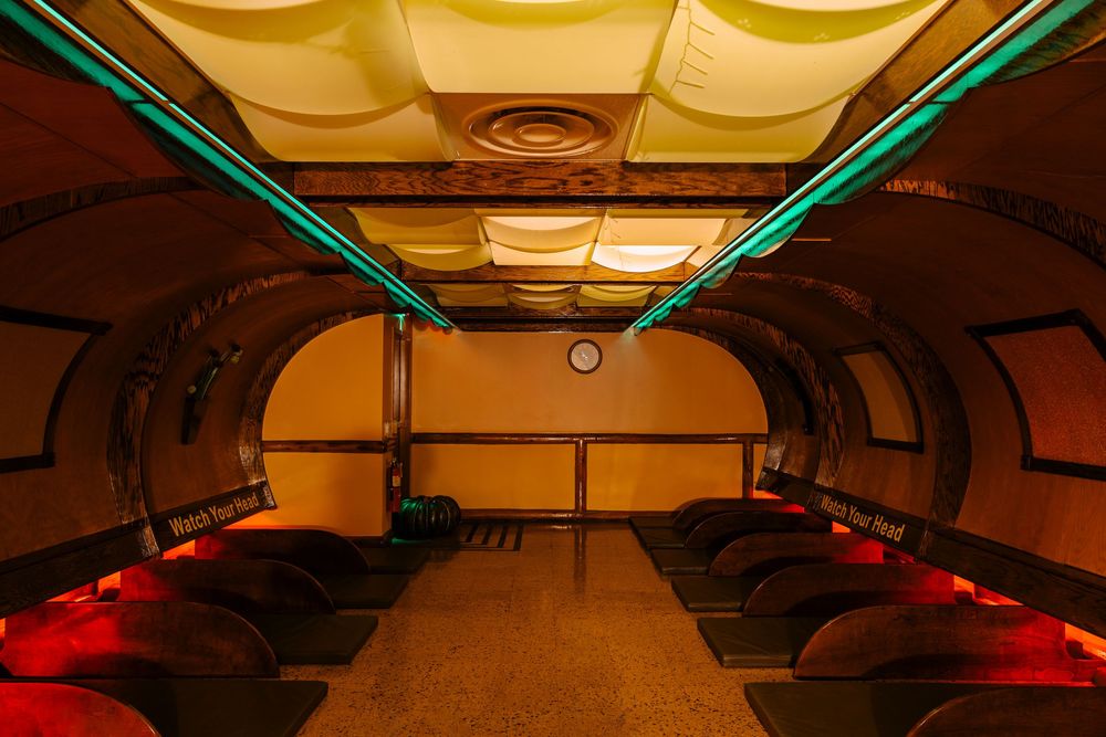 Art deco underground tunnel bar with curved ceiling, neon lighting, and rows of dark seating in warm amber tones.
