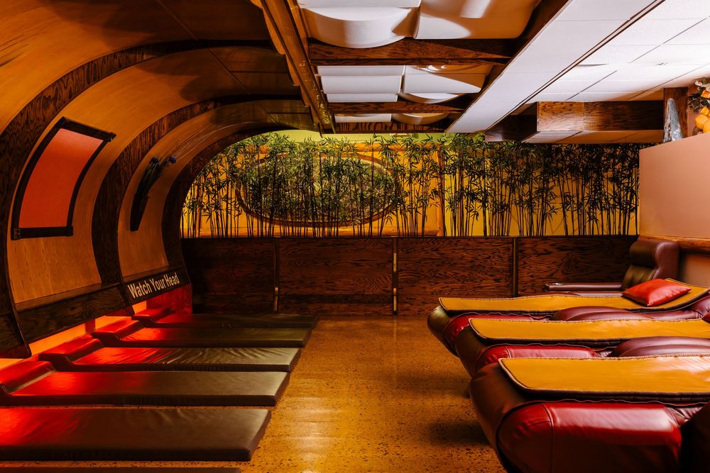 Cozy lounge with arched ceiling, red cushioned beds, and a bamboo forest mural in warm ambient lighting.