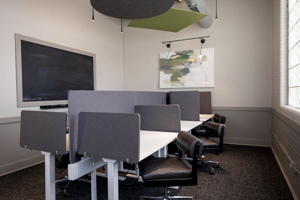 Modern conference room with gray partition desks, black leather chairs, a wall-mounted TV, and decorative acoustic ceiling panels.