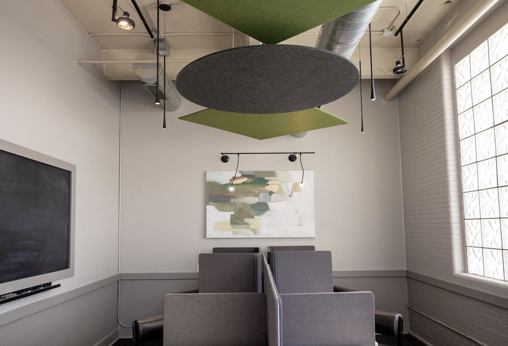 Modern conference room with gray chairs, abstract wall art, and green acoustic ceiling panels for sound management.