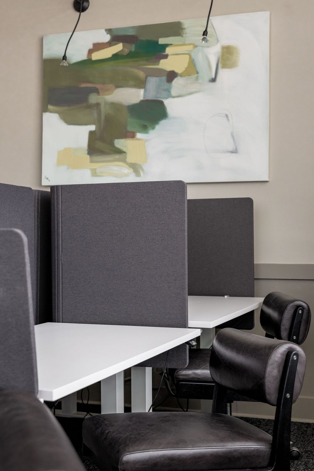 Modern office workstations with gray dividers, white desks, black leather chairs, and abstract green wall art.