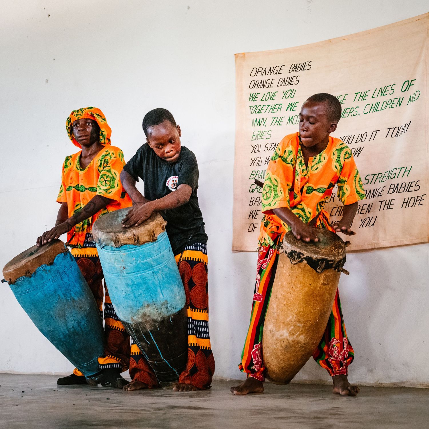 African children in colorful traditional attire playing large drums during a vibrant cultural performance.