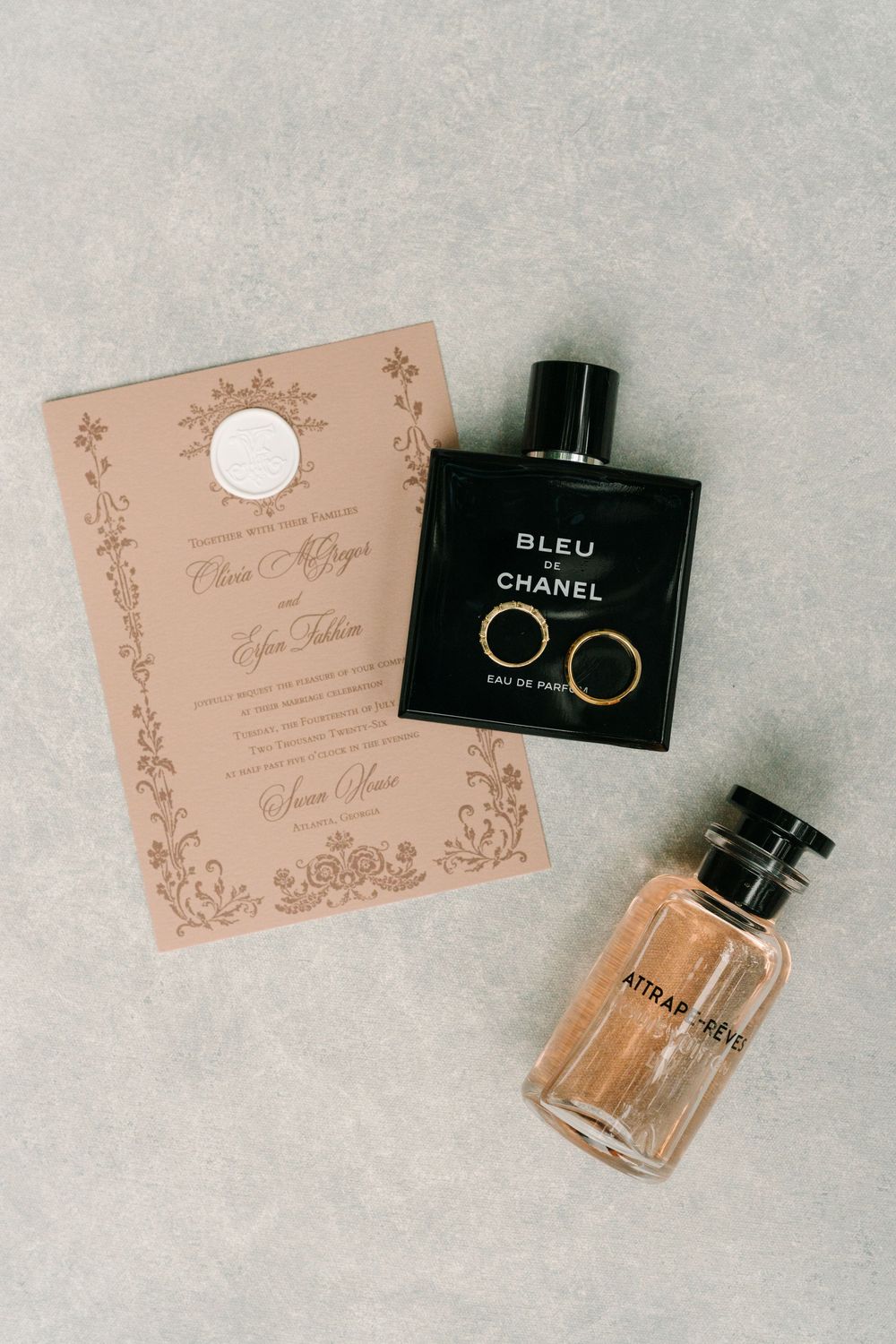 Wedding flat lay with Bleu de Chanel cologne, Louis Vuitton perfume, gold rings, and elegant blush invitation.