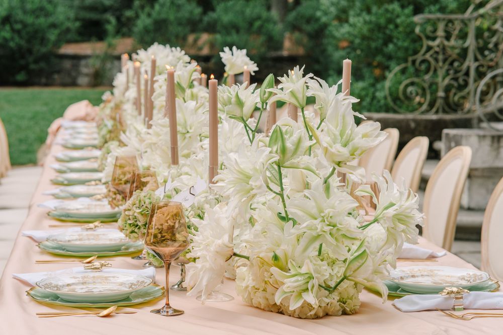 Elegant outdoor wedding reception table with white lily centerpieces, tall taper candles, and green charger plates.