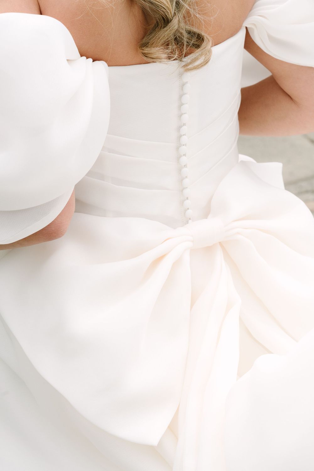 Close-up of a bridal gown back featuring elegant buttons, puff sleeves, and a large satin bow detail.