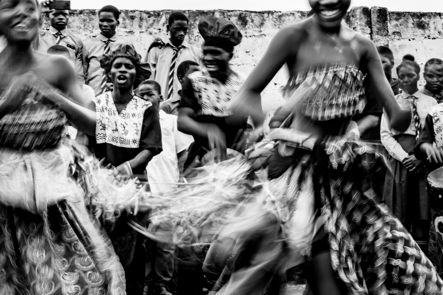 Black and white photo of African women in traditional attire dancing energetically at a cultural celebration.