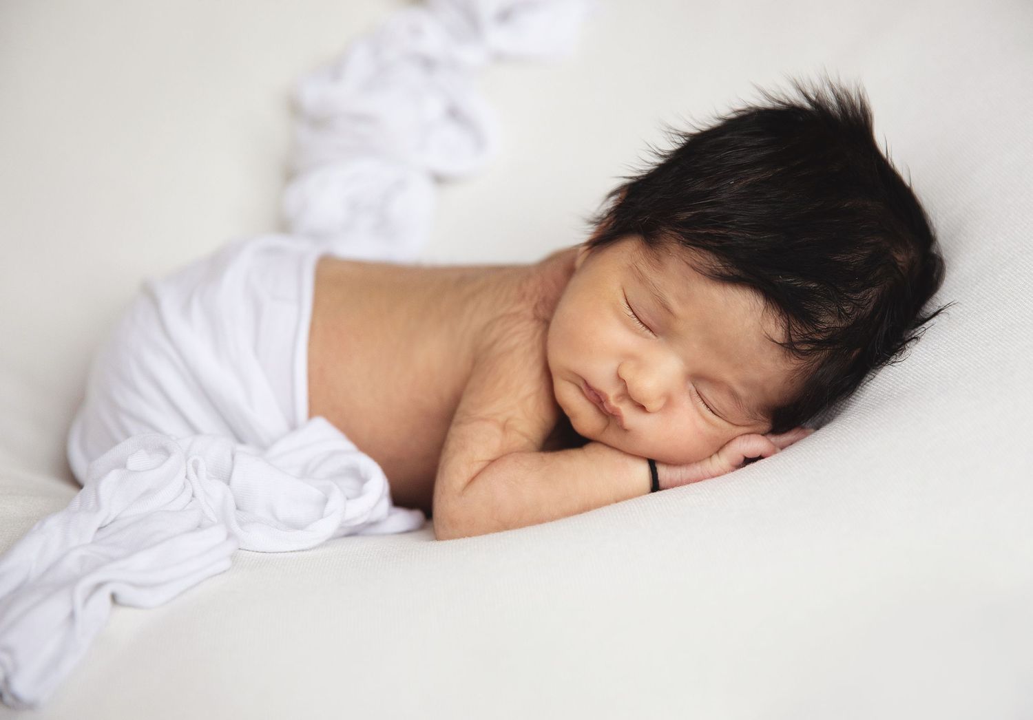 Peaceful newborn baby sleeping wrapped in white cloth with dark hair, perfect newborn photography portrait in South East London