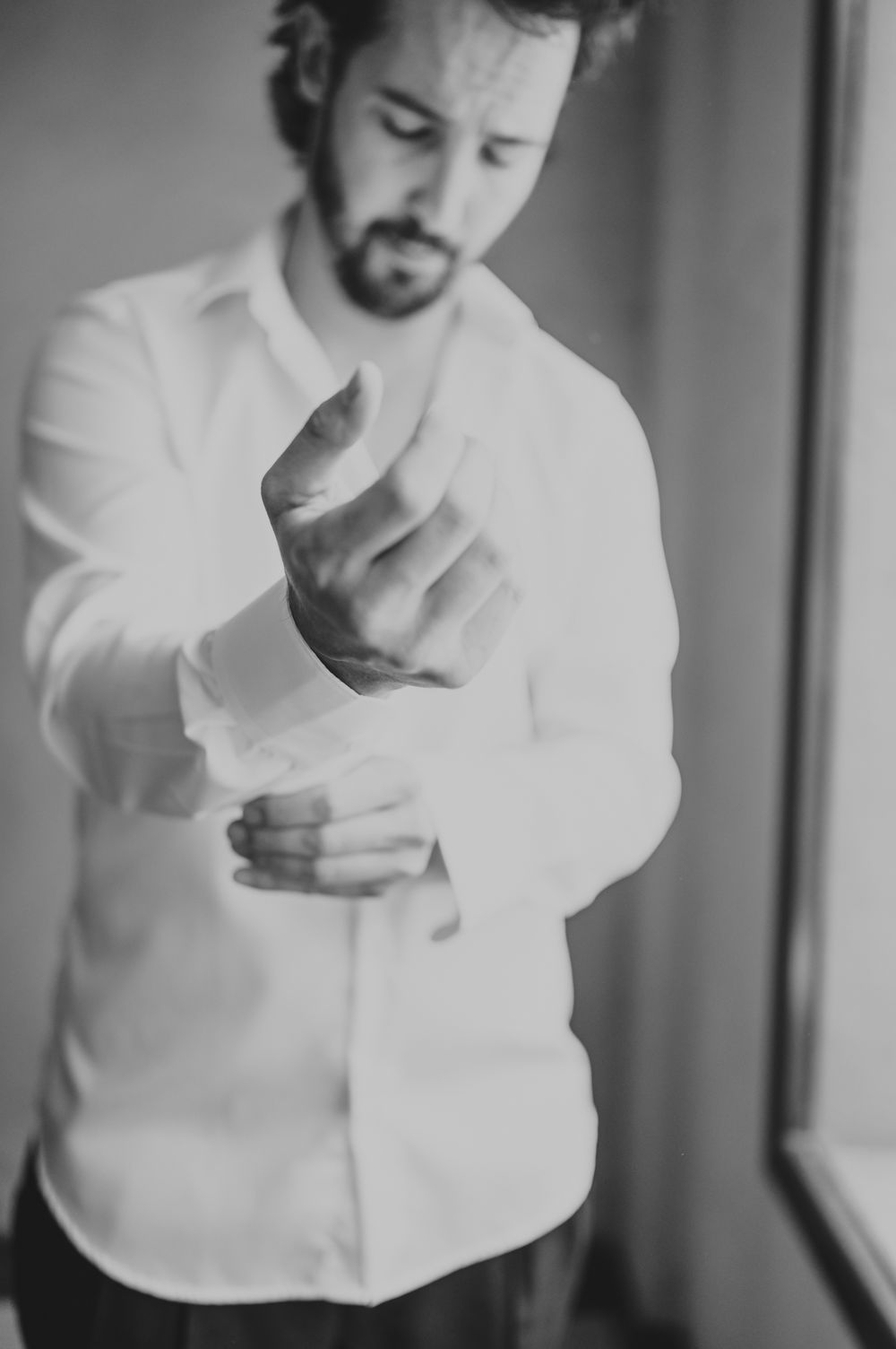 Groom adjusting his shirt cuffs in a black and white wedding preparation photo.