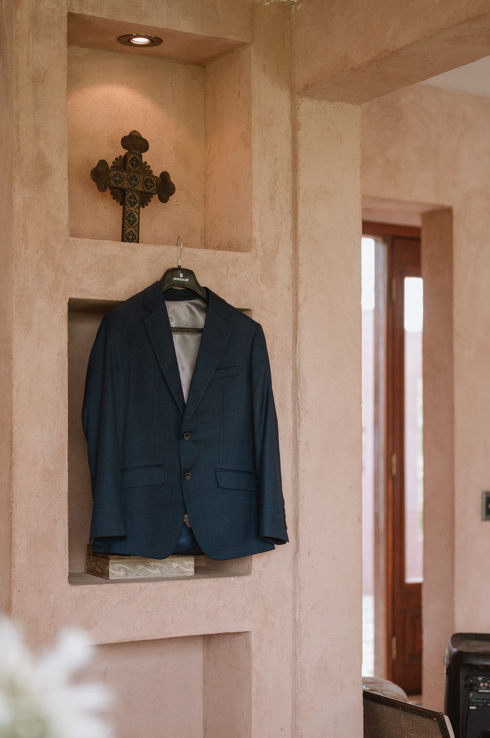 Navy blue groom suit jacket hanging in a rustic niche with a decorative cross above.