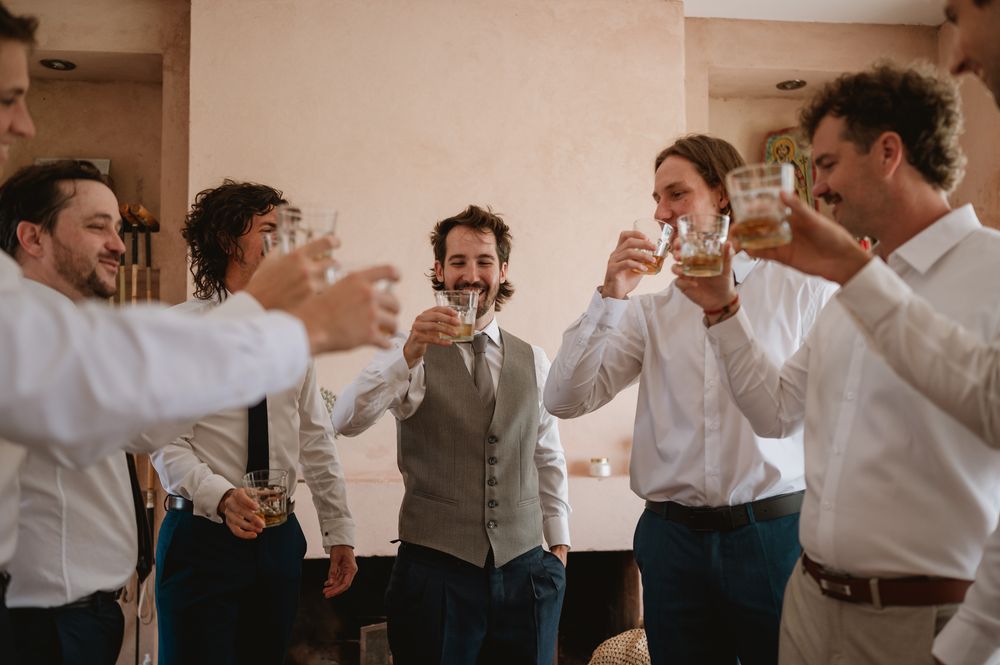 Groom and groomsmen raising glasses in a joyful whiskey toast before the wedding.