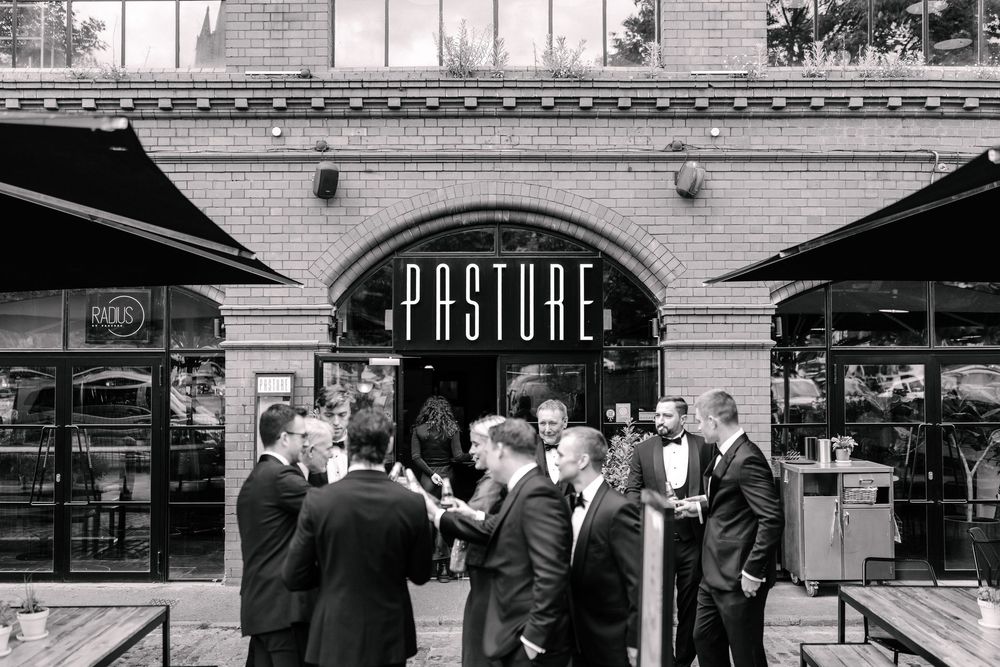 Black and white photo of elegantly dressed guests socializing outside Pasture restaurant Bristol, a brick building with awnings.