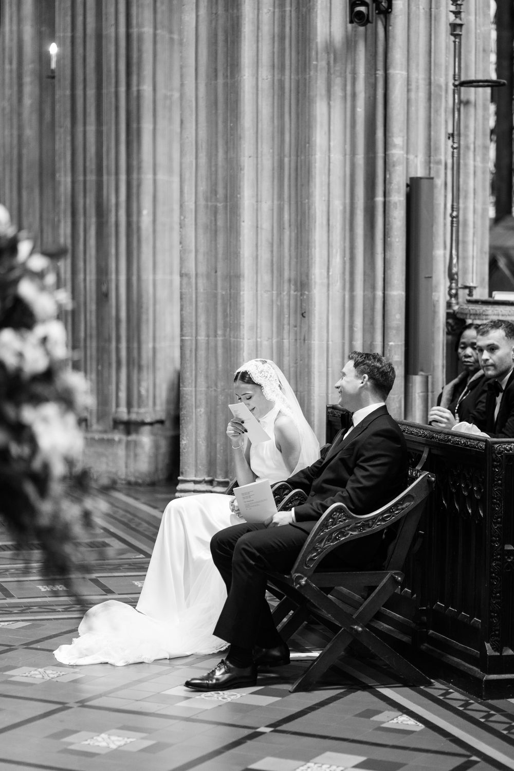 Black and white image of bride and groom seated in grand cathedral during wedding ceremony at St Mary Redcliffe Church, Bristol Wedding