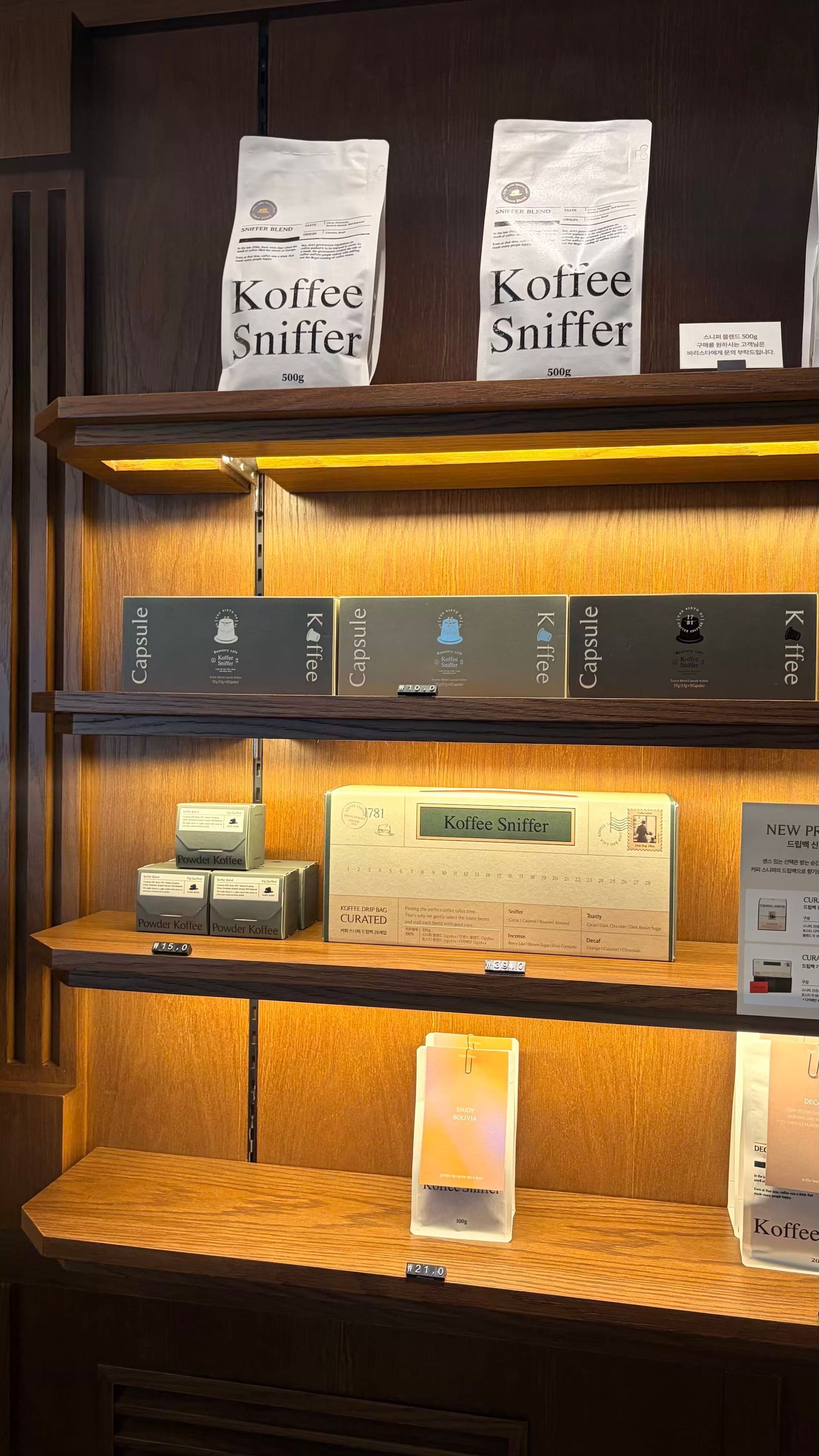 Koffee Sniffer branded coffee bags and capsule boxes displayed on illuminated wooden retail shelves.