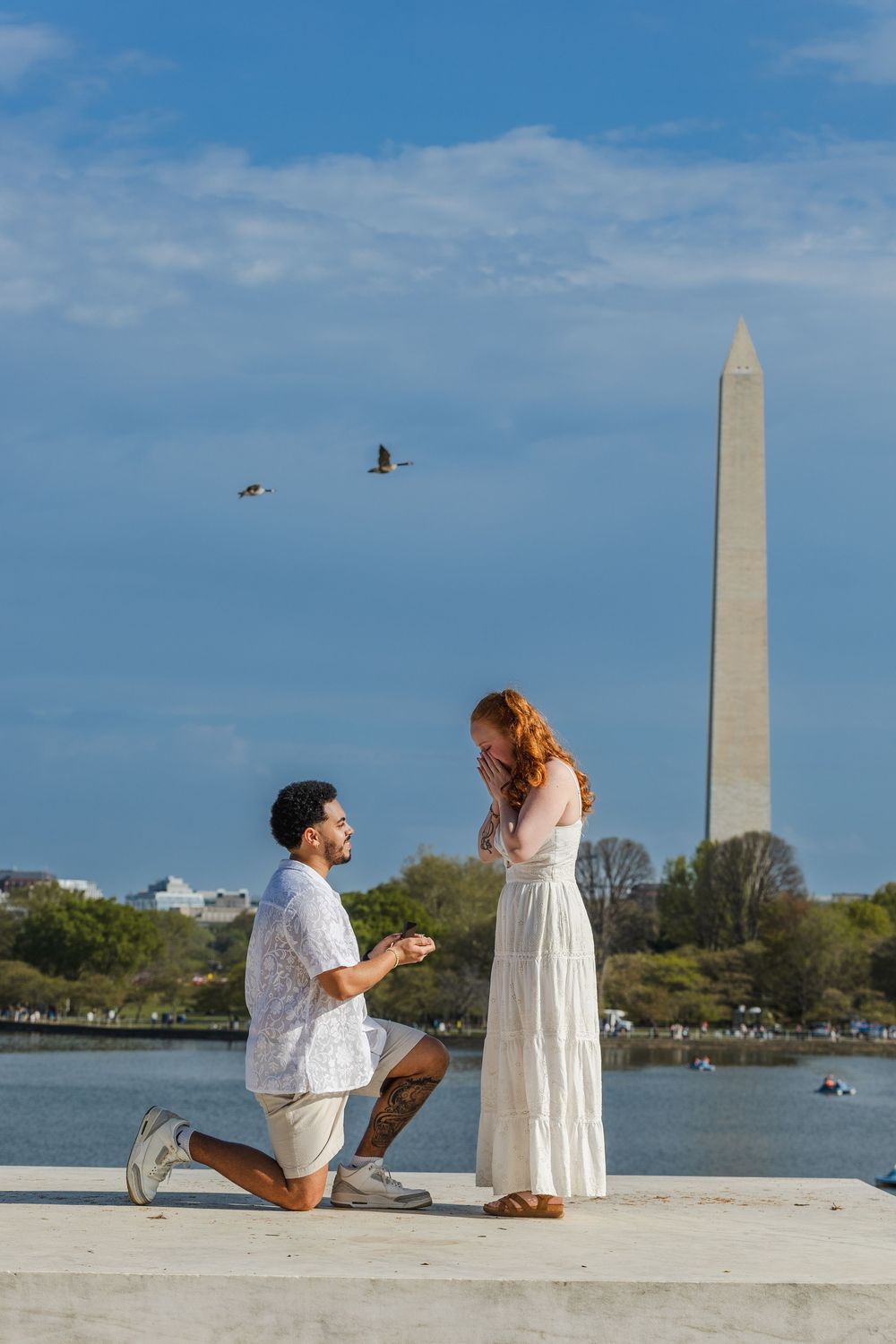 Man proposing on one knee to a woman in a white dress near the Washington Monument in Washington DC.