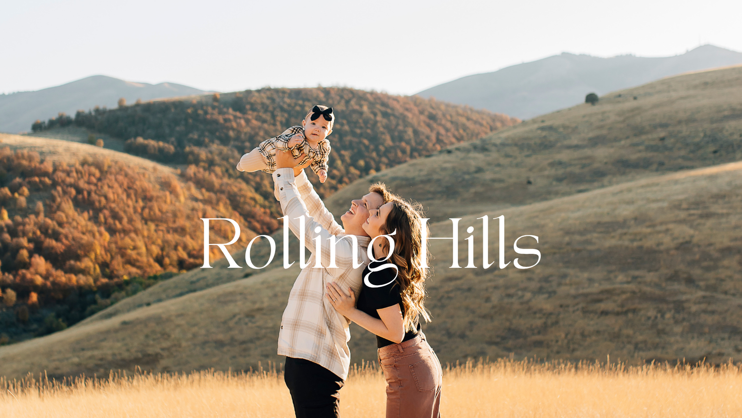 Couple lifting baby in golden rolling hills landscape during autumn family photo session outdoors.