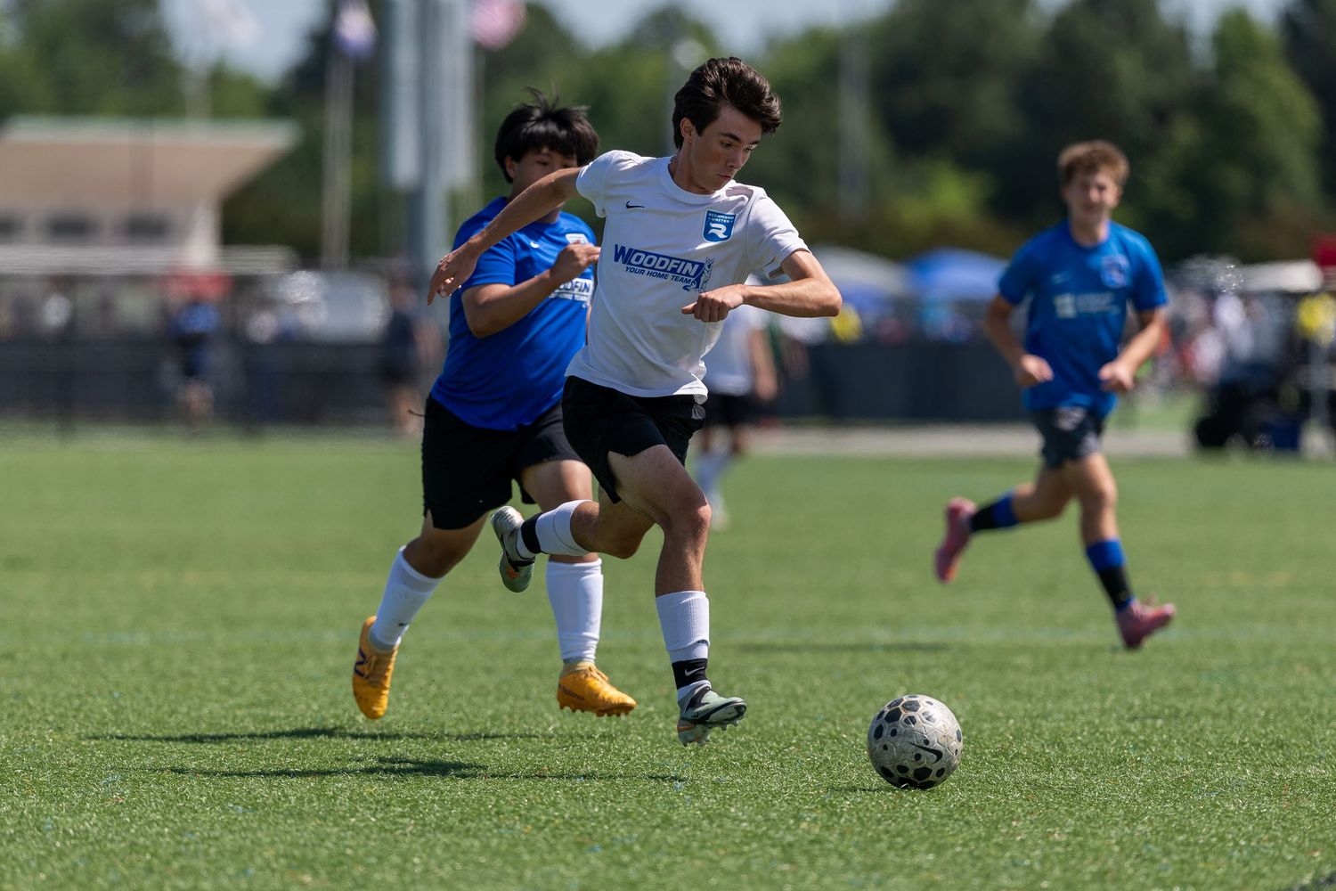 Two youth soccer players compete for the ball during a sunny outdoor match on a green grass field.