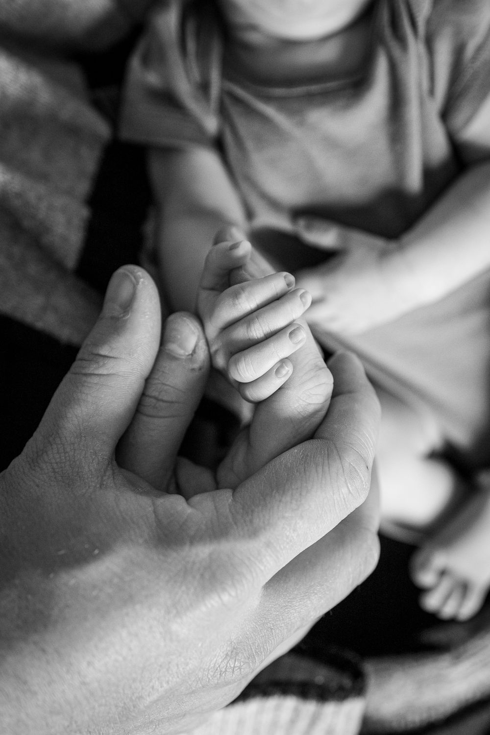 Black and white photo of a baby grasping an adult finger, symbolizing family bond and new parenthood.