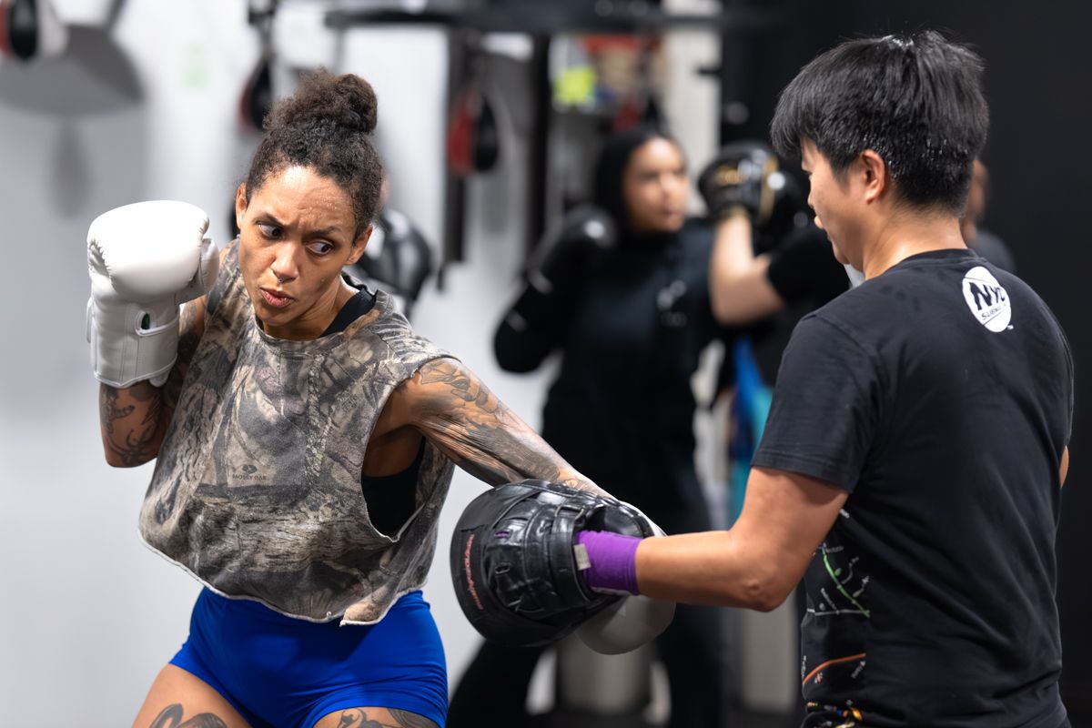 Boxer throws a punch at trainer holding pads in gym during boxing training session.
