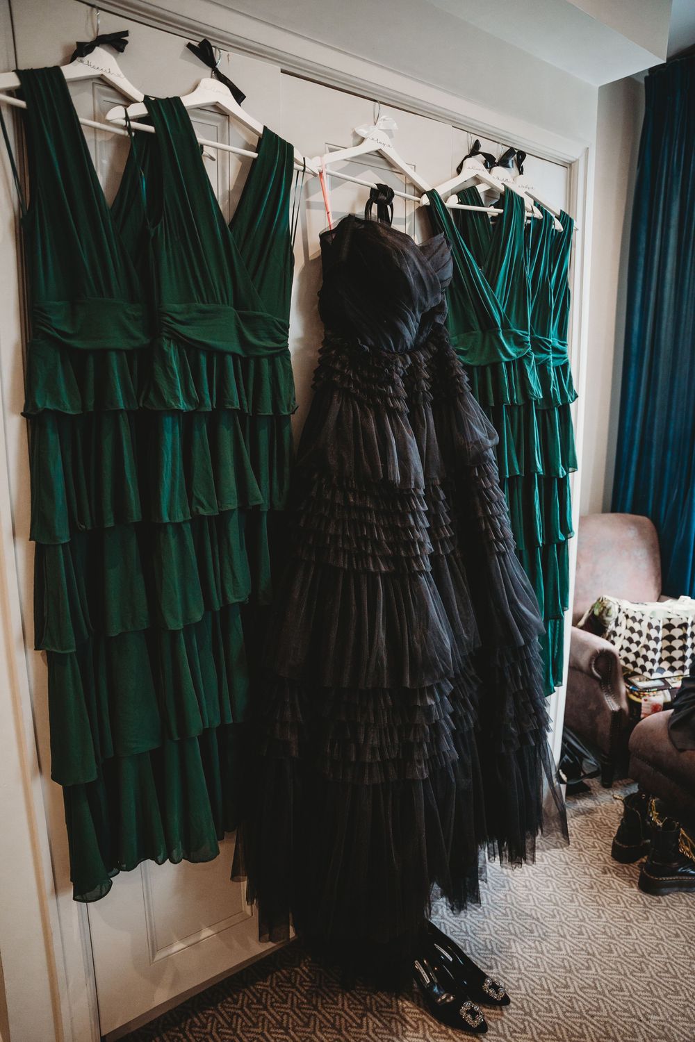 Black tiered wedding gown hangs beside emerald green bridesmaid dresses on a door.