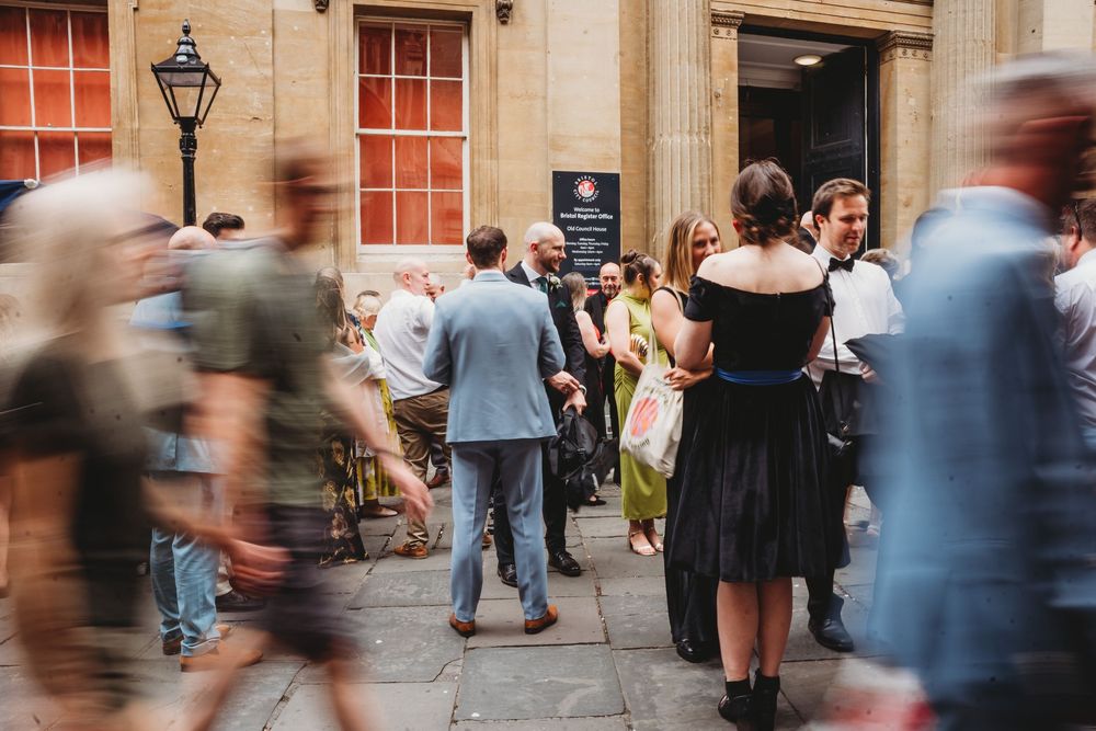 Blurred motion photo of wedding guests mingling outside grand stone building.