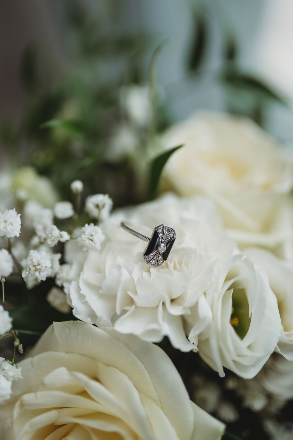 An elegant diamond engagement ring displayed on white roses and baby's breath in a bridal bouquet.