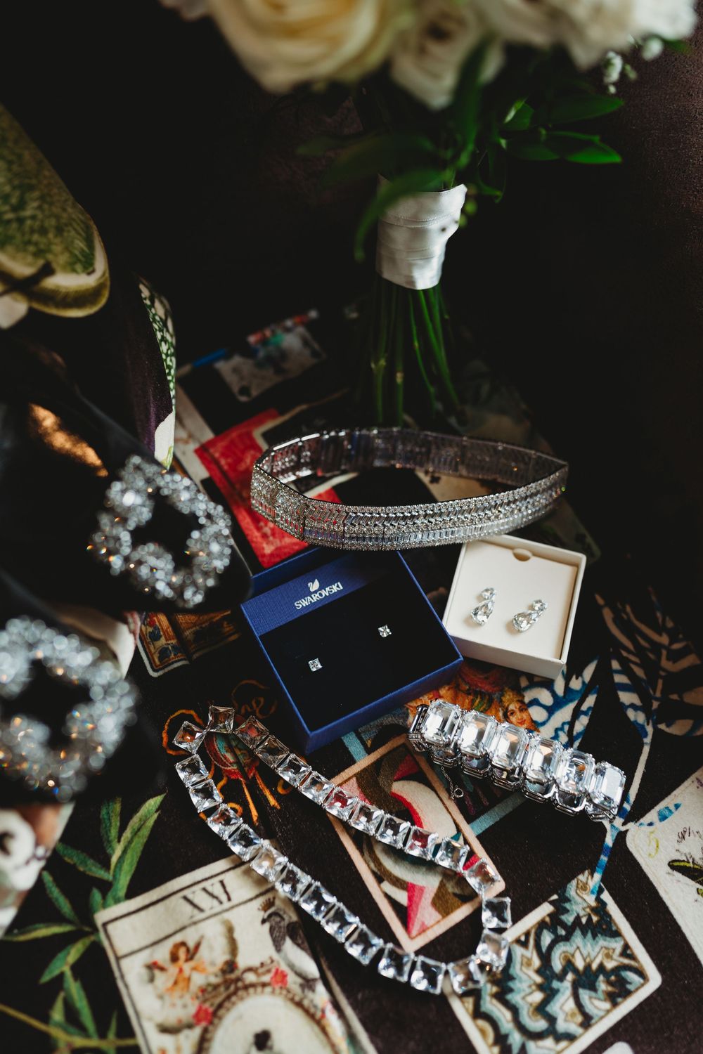 Crystal bridal jewelry flatlay featuring Swarovski earrings, tiara, bracelet, and necklace arranged on dark surface.
