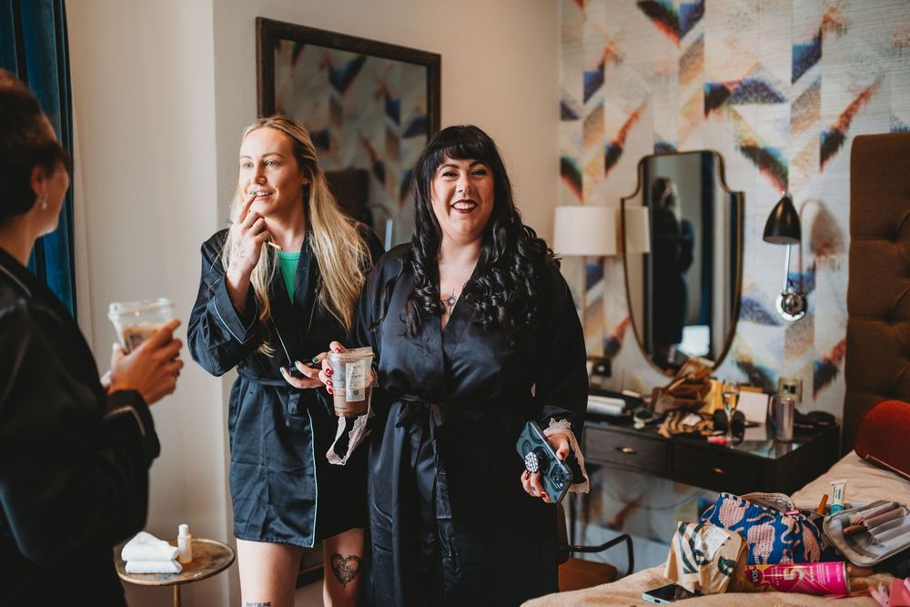 Bride and bridesmaid laughing in robes during fun wedding morning preparations.