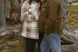 Couple embracing by a tree, woman in brown plaid coat, man in olive Carhartt jacket and jeans.