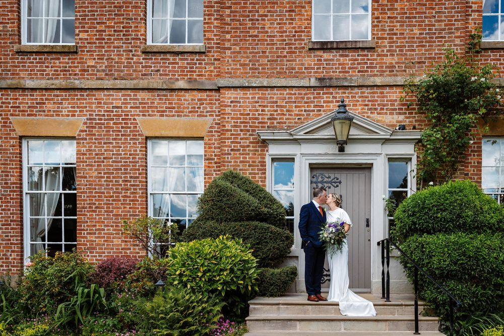Bride and groom share a kiss on the steps at Rivington Hall Barn captured by Lynette Matthews Photography