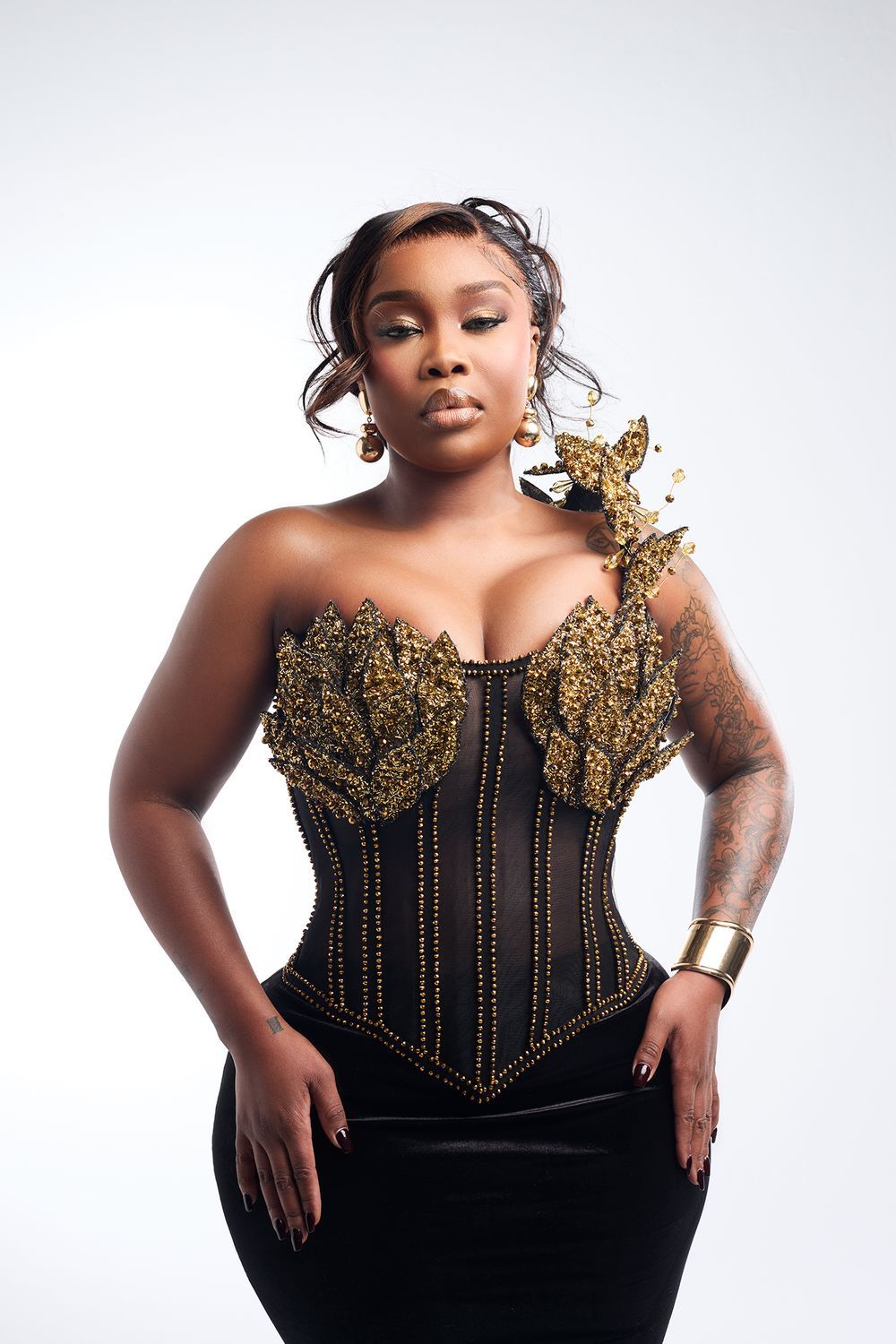 Woman wearing black and gold embellished corset top with arm cuff in studio.