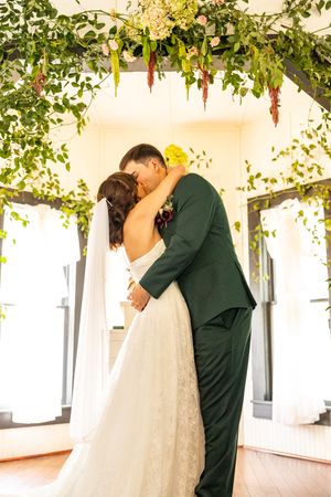 Bride and groom sharing first kiss under lush floral arch at outdoor wedding ceremony.