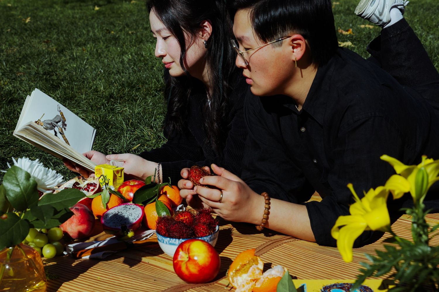 A couple picnicking in the grass, surrounded by different fruits and flowers at the Lewis MacAdams Riverfront Park in Los Angeles.