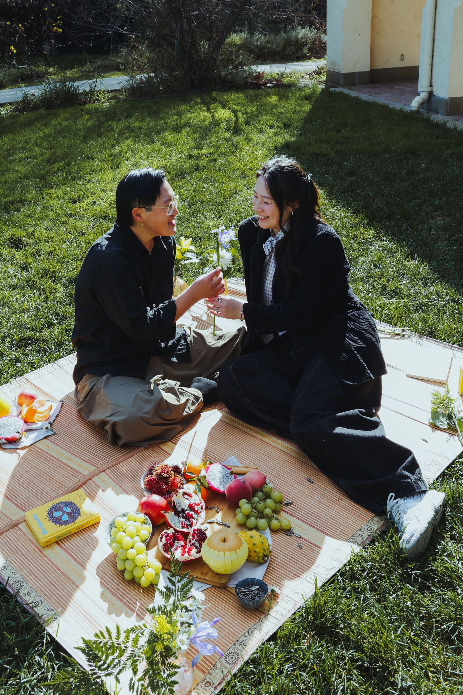 A couple picnicking in the grass, surrounded by different fruits and flowers at the Lewis MacAdams Riverfront Park in Los Angeles.