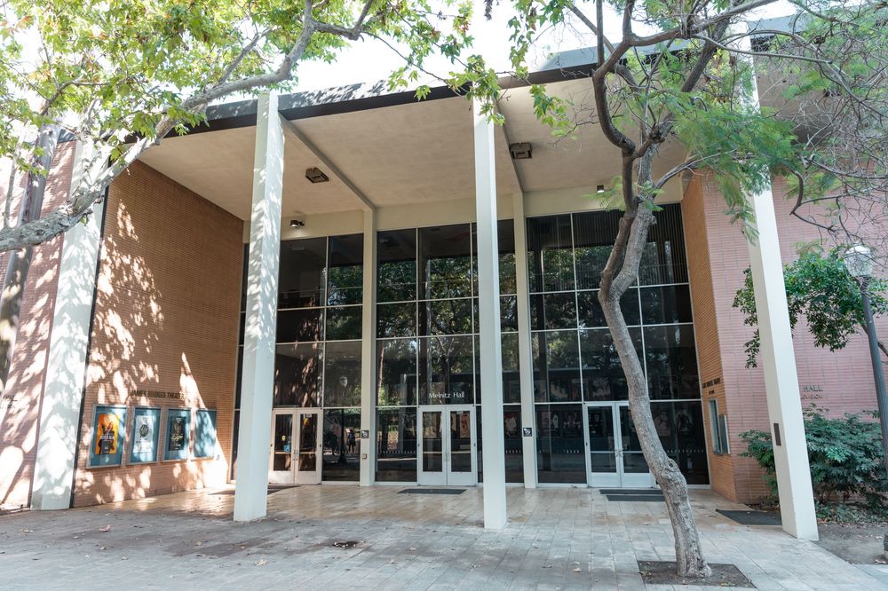 Modern building entrance with tall white columns, glass doors, and surrounding trees on a sunny day.