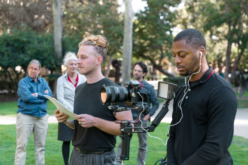 Two filmmakers on a film set outdoors, one holding a camera gimbal while reviewing notes in a park.