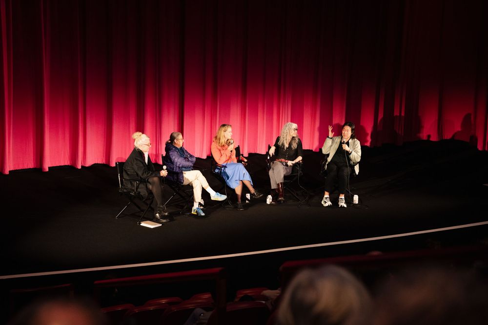 Five panelists seated on stage before a red curtain during a Q&A discussion at a film screening event.