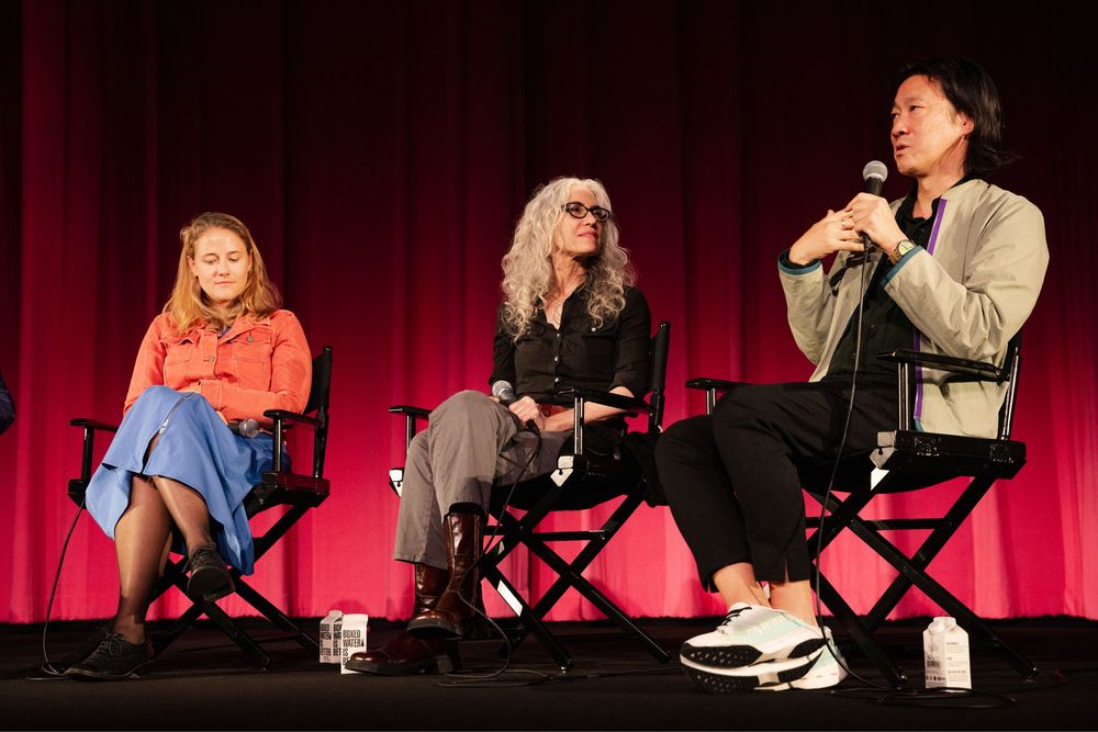 Three panelists seated in director chairs on a stage with red curtains during a Q&A discussion event.